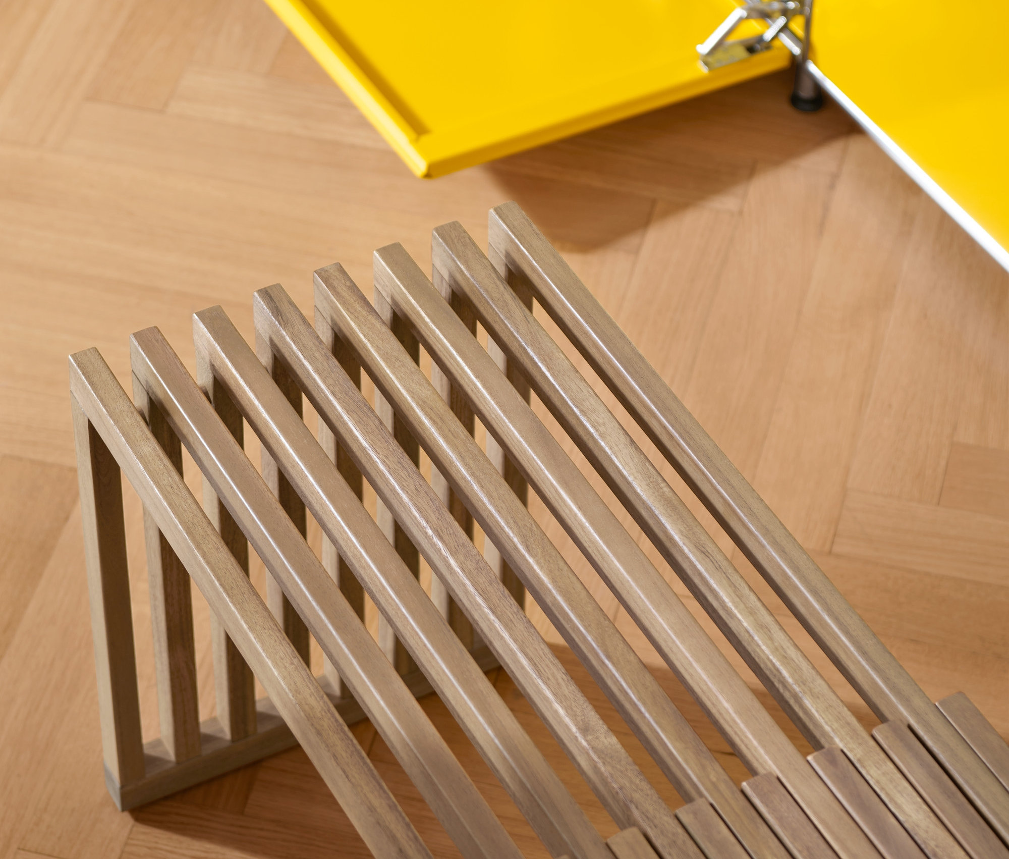 Közelkép egy kihúzható pad és egy sárga szekrény részletéről parkettás padlón.