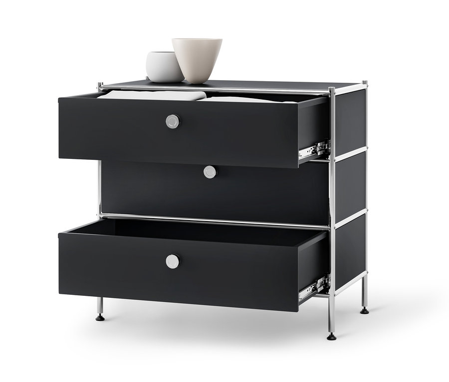 Fekete »CN3« fém komód 3 fiókkal, melyből kettő nyitva van, a tetején pedig két váza található.