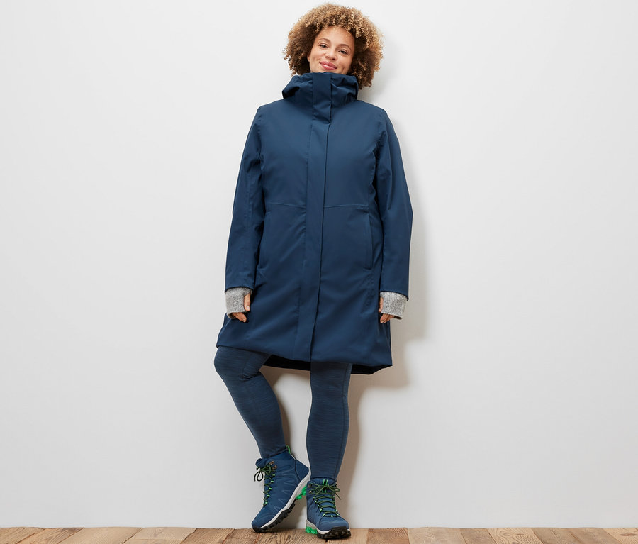 Nő pózol sötétkék melírozott sportnadrágban és 3 az 1-ben funkcionális kabátban.