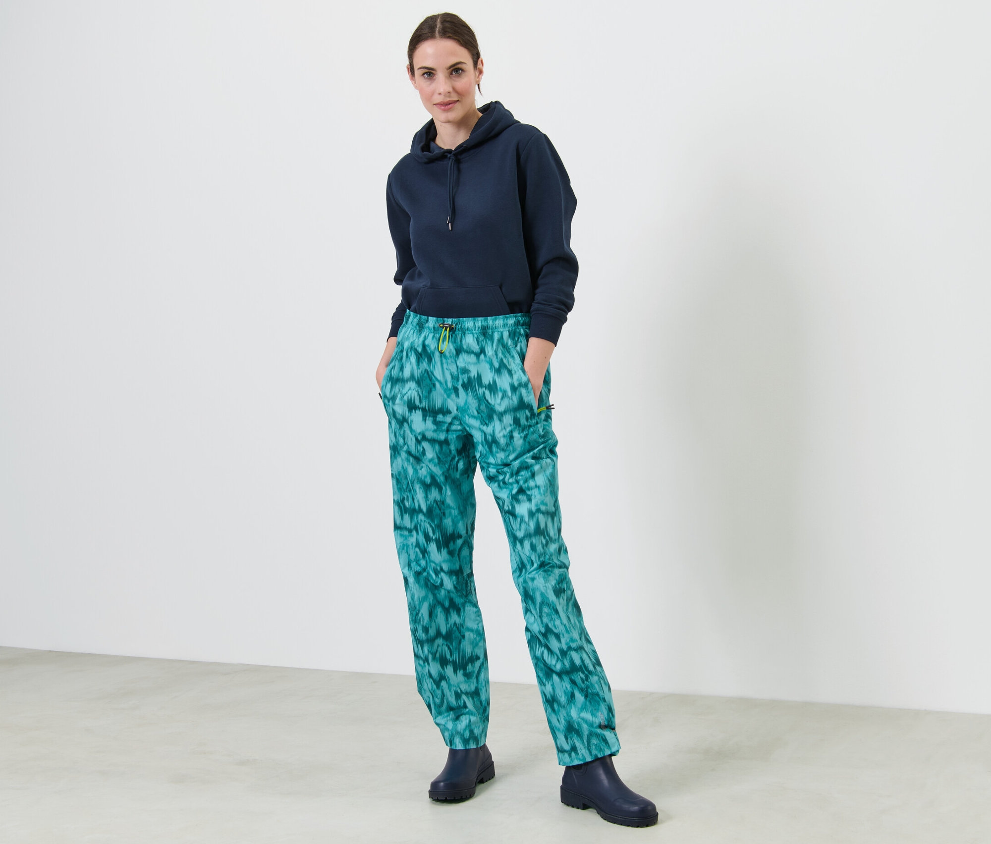 Egy nő áll, kezével a mintás esőnadrág zsebében.