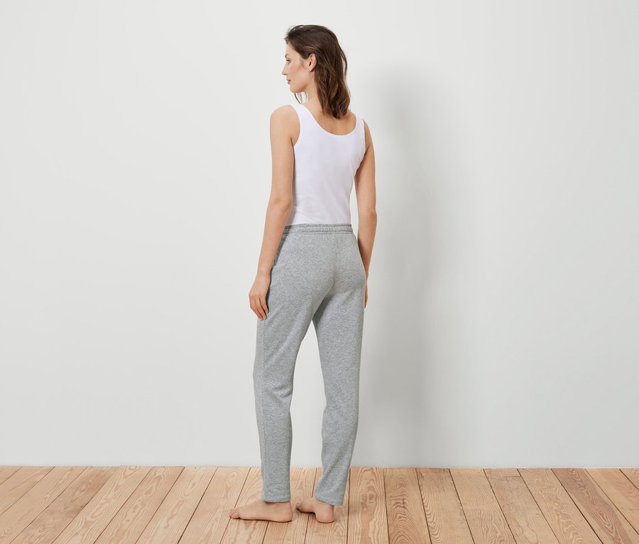 Egy nő háttal áll a kamerának, fehér trikót és szürke joggingalsót visel.