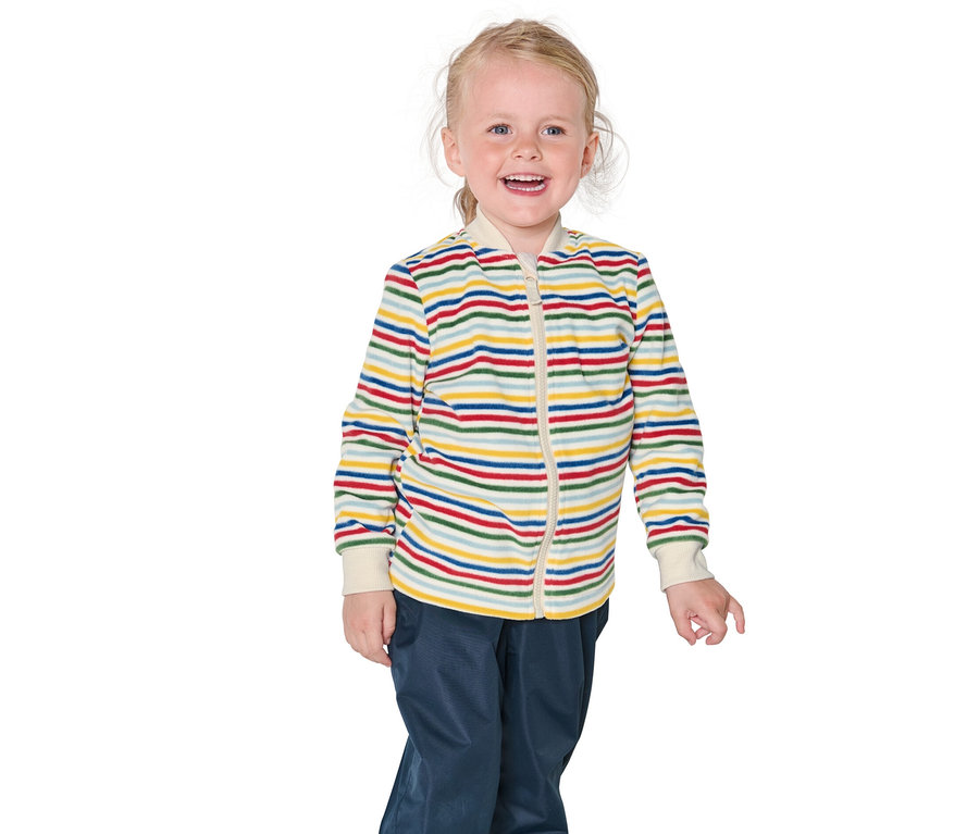 Egy mosolygós szőke kislány csíkos kabátot és kék nadrágot visel.