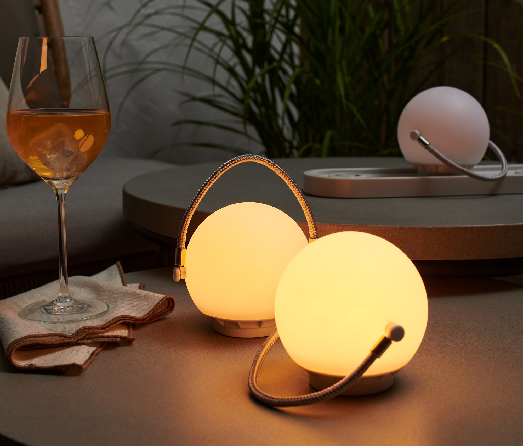 Az asztalon egy akkumulátoros asztali lámpa szett áll egy ital mellett.