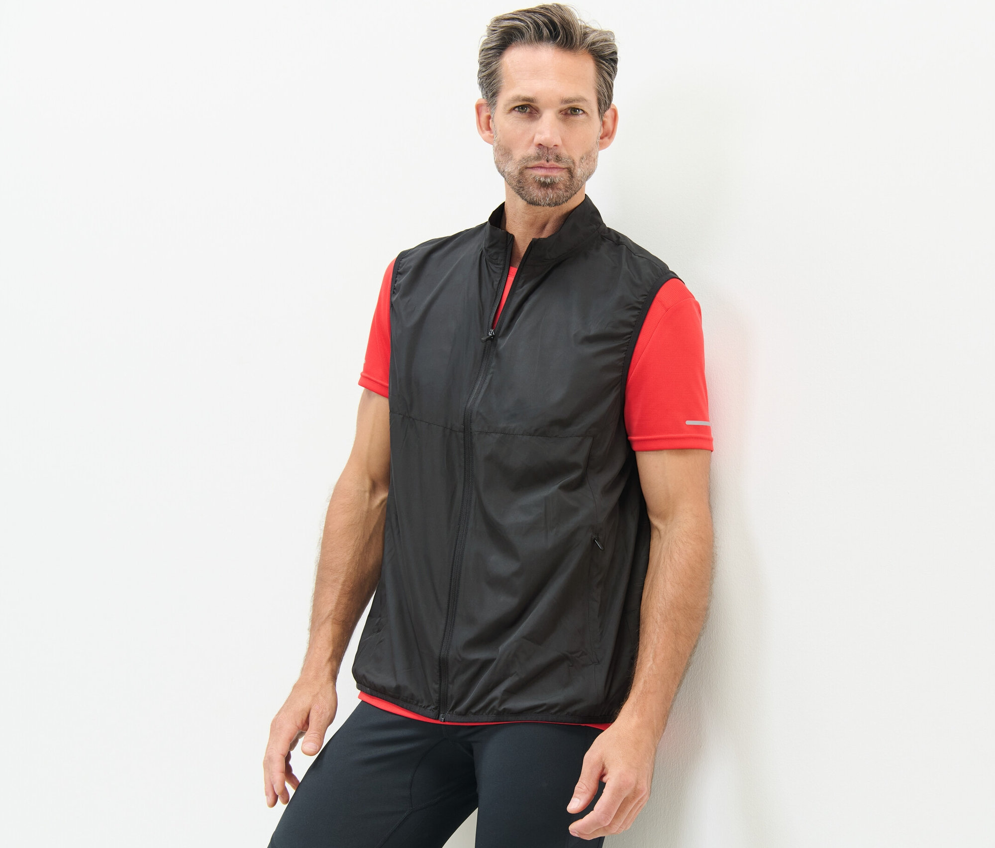 Férfi a falnak támaszkodva, fekete funkcionális mellény van rajta.