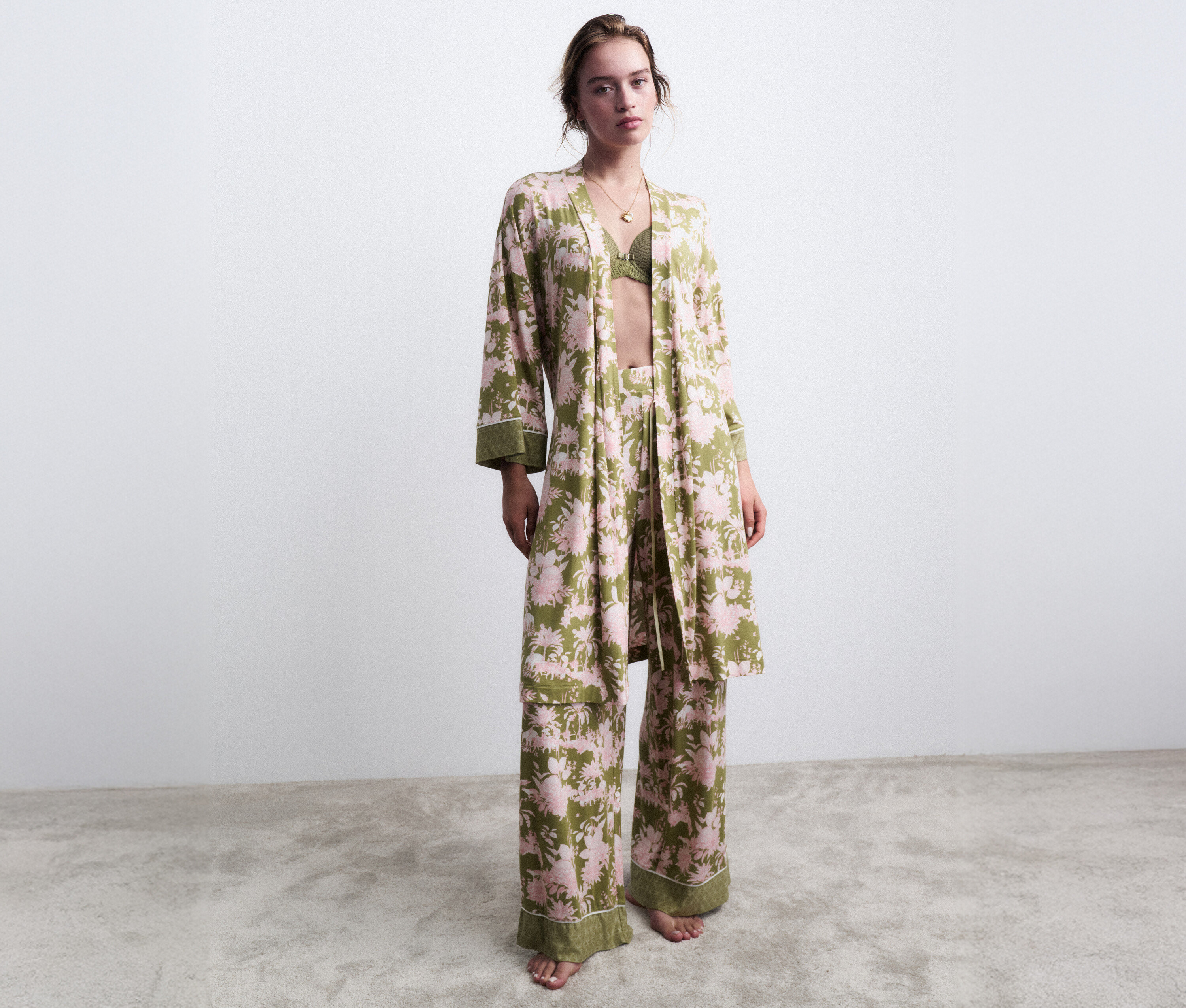 Nő áll mezítláb zöld, virágmintás pizsamában hozzáillő köntössel.