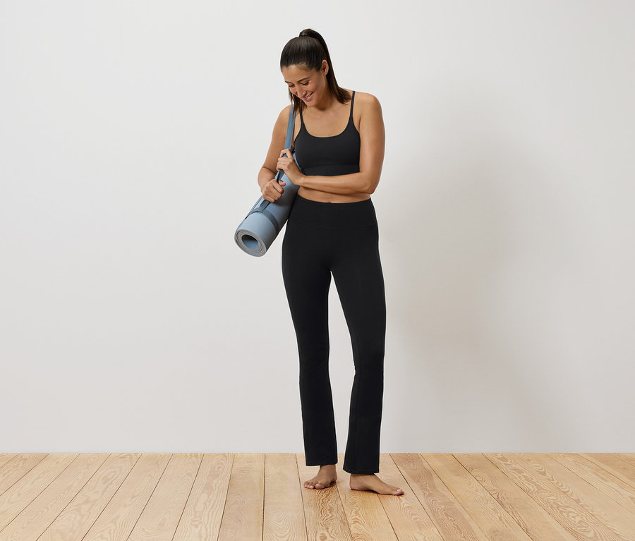 Nő fekete sportruházatban jógamatracot tart.