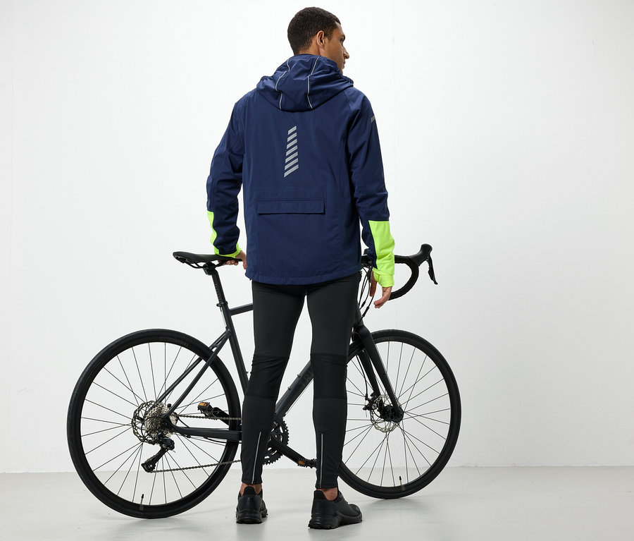 Kapucnis kabátos férfi áll a kerékpár mellett.