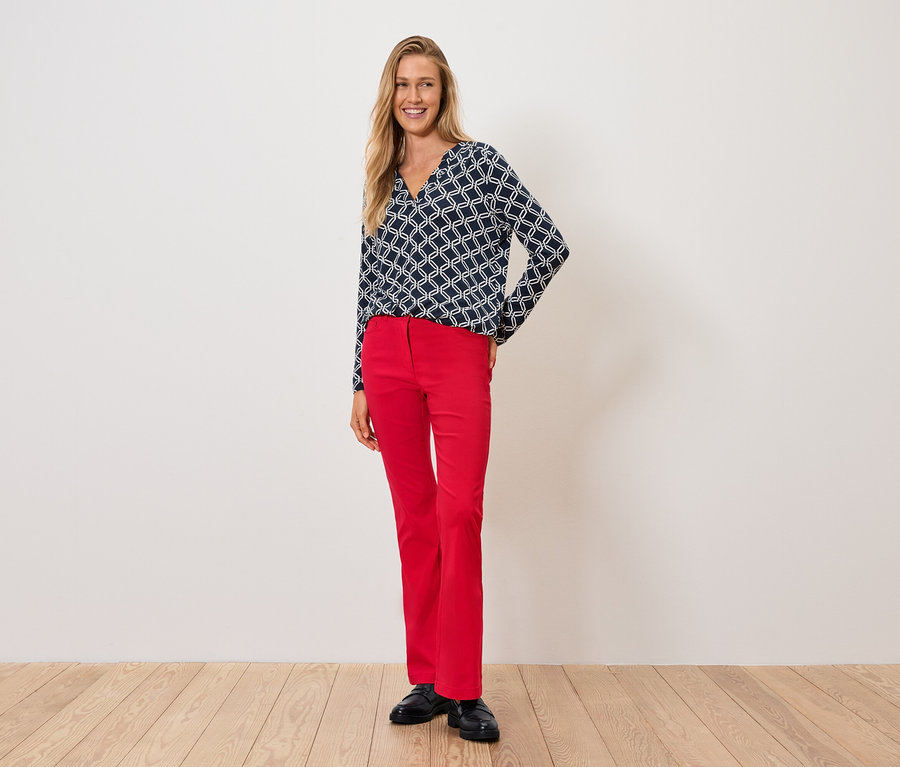 Nő kék-fehér felsőben és piros nadrágban áll a fapadlón.