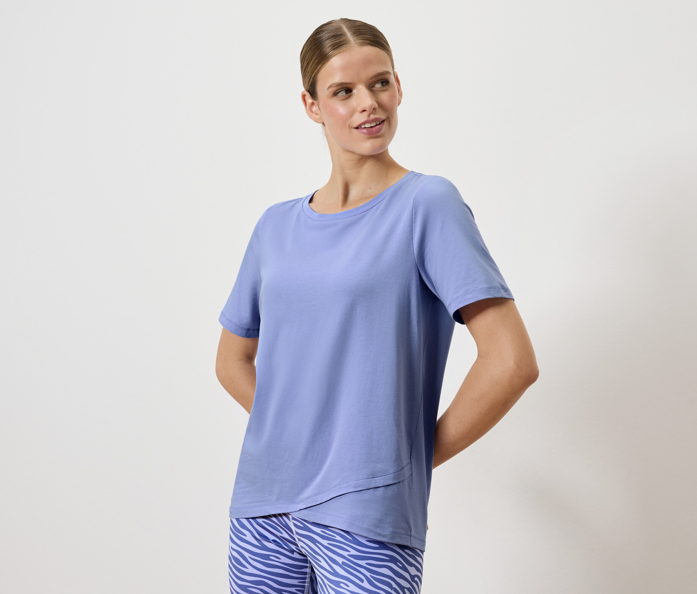 Nő pózol kék pólóban és állatmintás nadrágban.