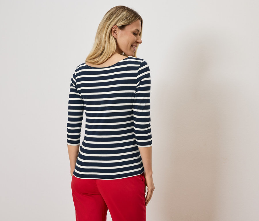 Szőke nő kék-fehér csíkos felsőben és piros nadrágban.