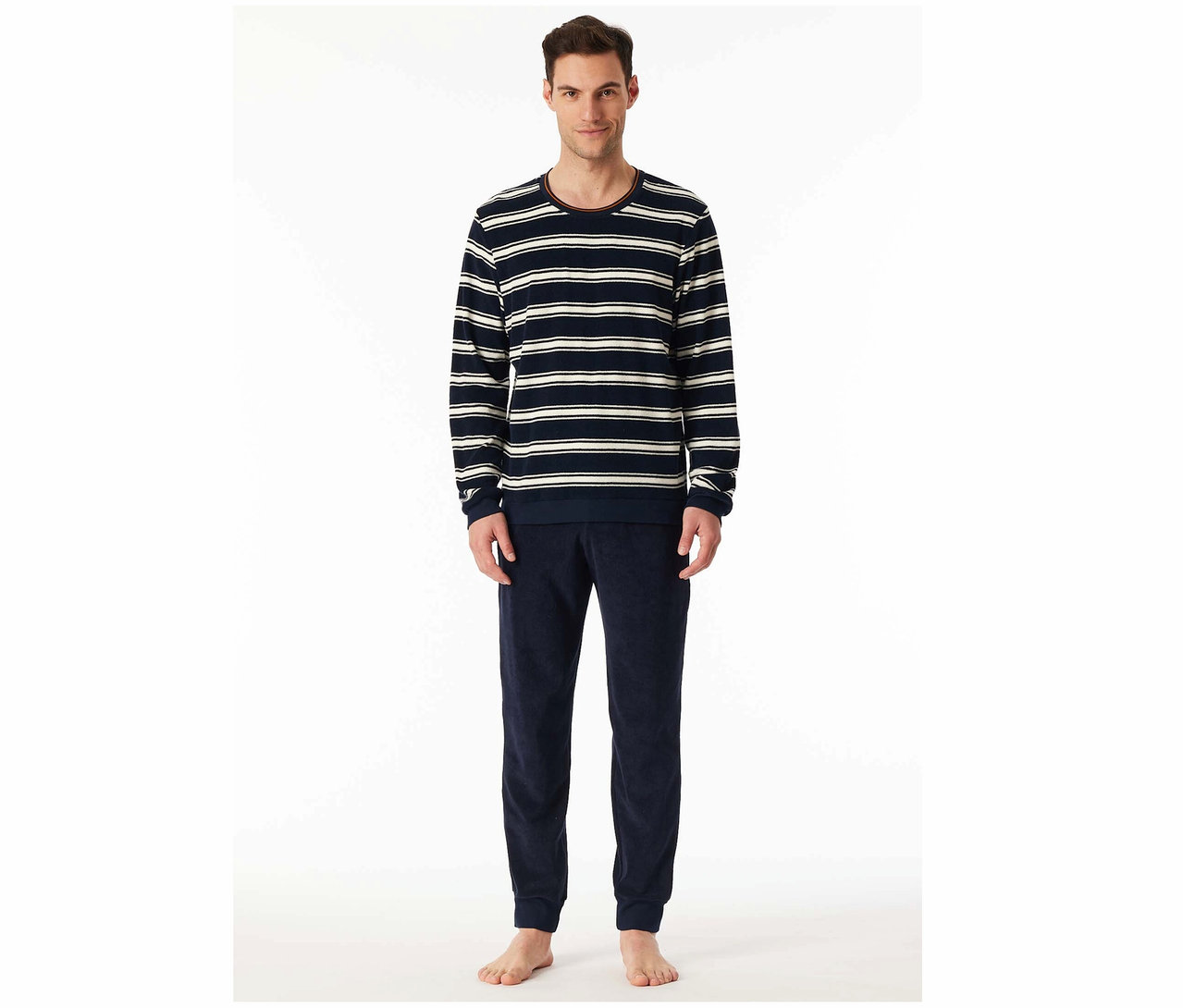 Egy férfi áll, és csíkos, hosszú ujjú felsőt és sötétkék bársony joggingalsót visel.