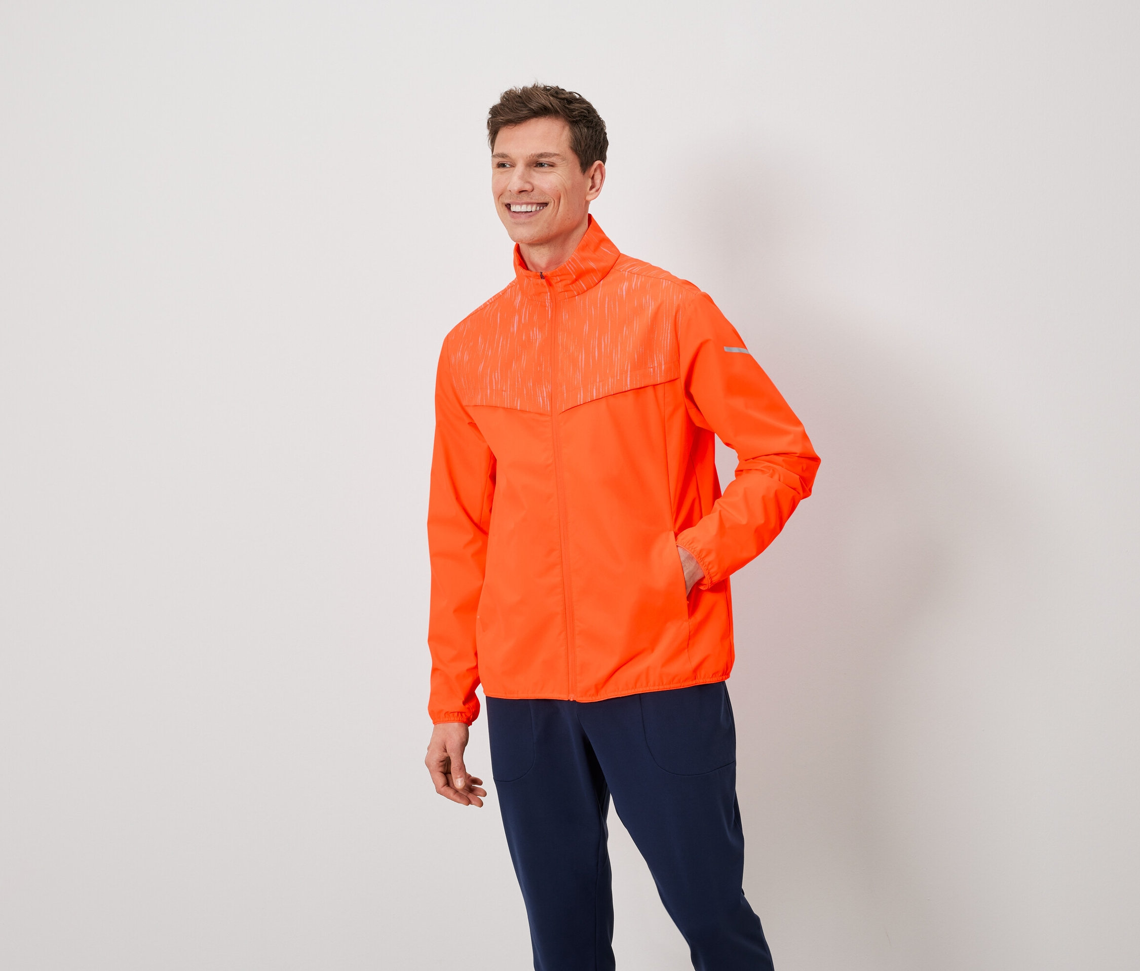 Egy barna hajú férfi narancssárga kabátot és sötétkék nadrágot visel.