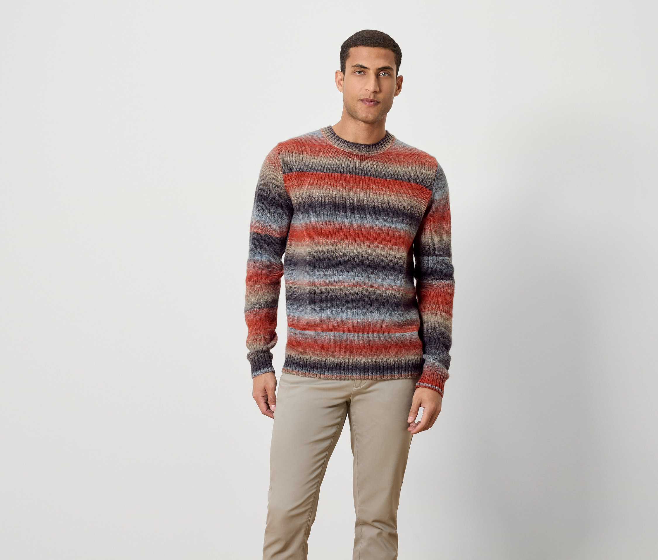 Egy férfi áll csíkos pulóvert és nadrágot viselve.