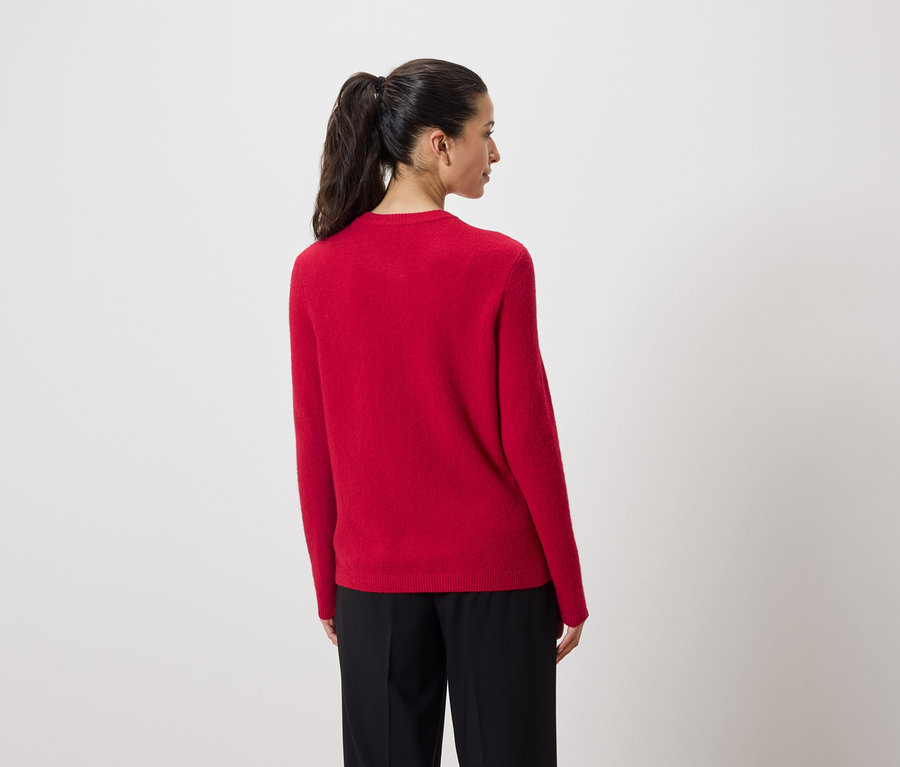 A kamerának háttal álló nő piros pulóvert és fekete nadrágot visel.