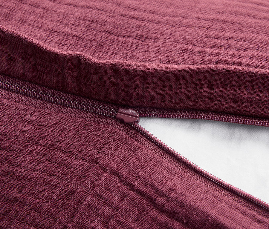 Egy bordó színű textilszövet részlete, nyitott cipzárral.