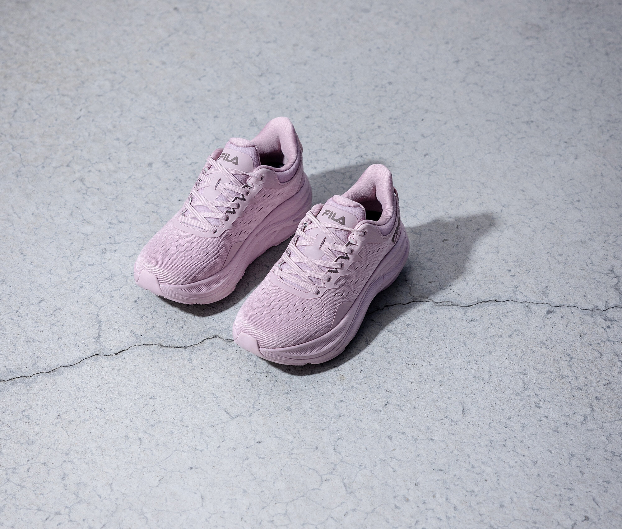 Két lila Fila futócipő áll egy szürke háttéren.