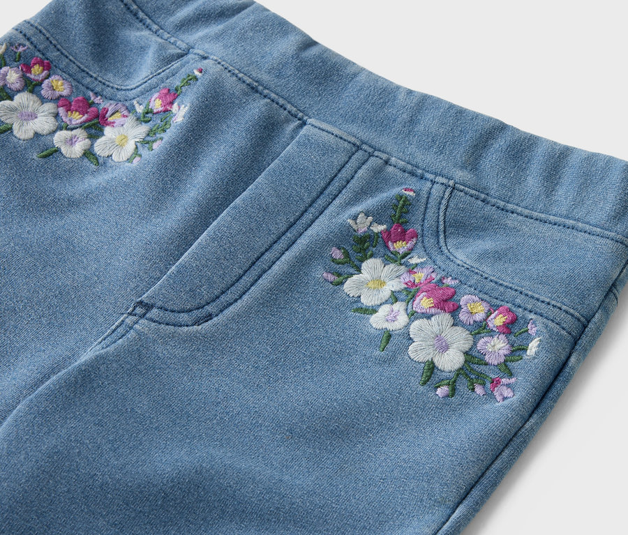 Kivilágított kép világoskék farmerről virágmintás hímzéssel a derékrészen és a zseben.