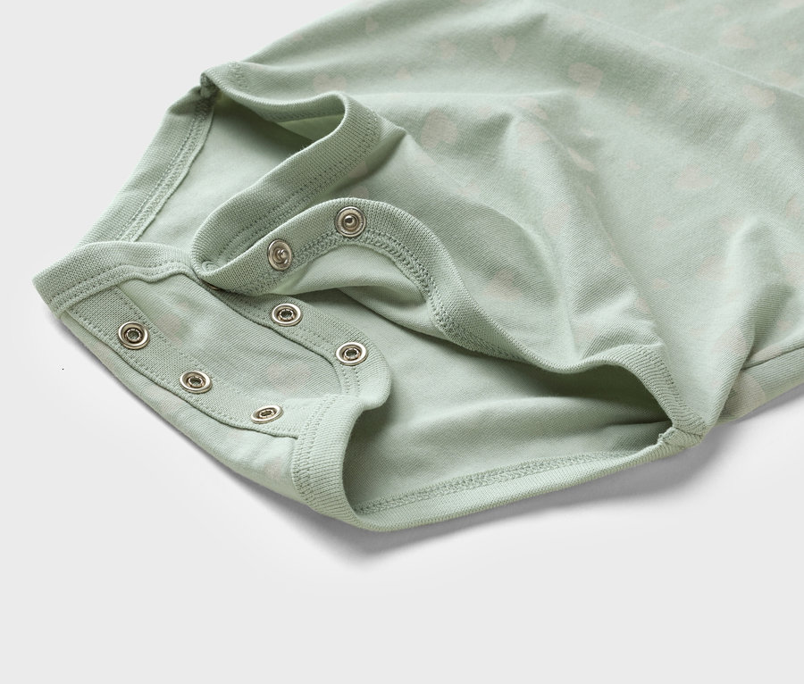 Közeli kép egy világoszöld, patentos babaruháról.