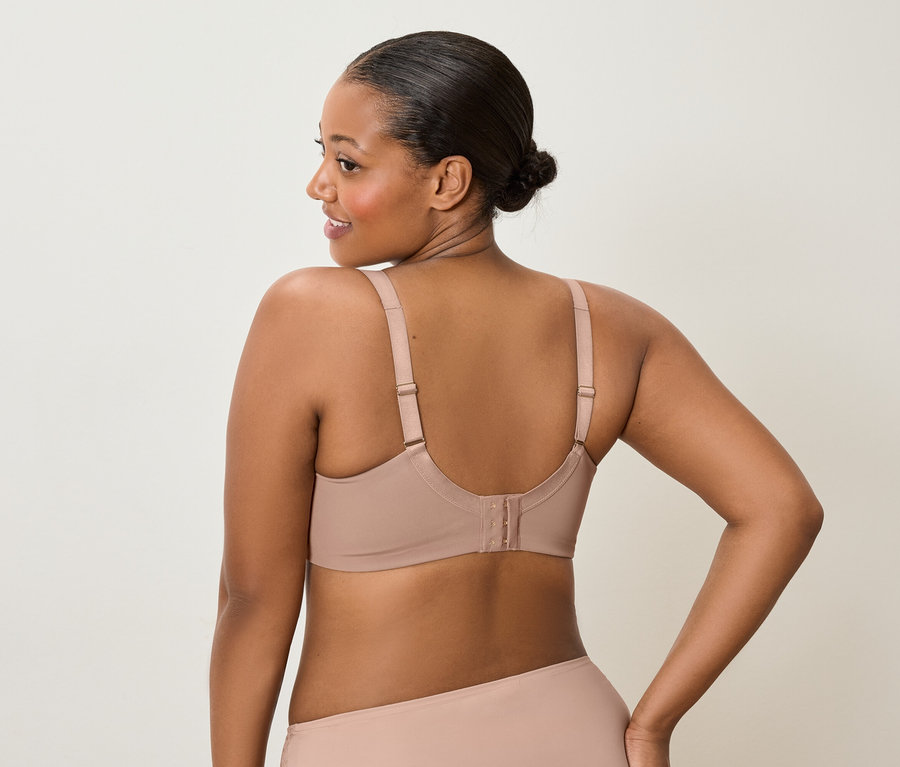 Hátulnézet egy sötét bőrű, kontyos nőről, aki bézs színű melltartót és hozzáillő alsóneműt visel, és a válla fölött balra néz.