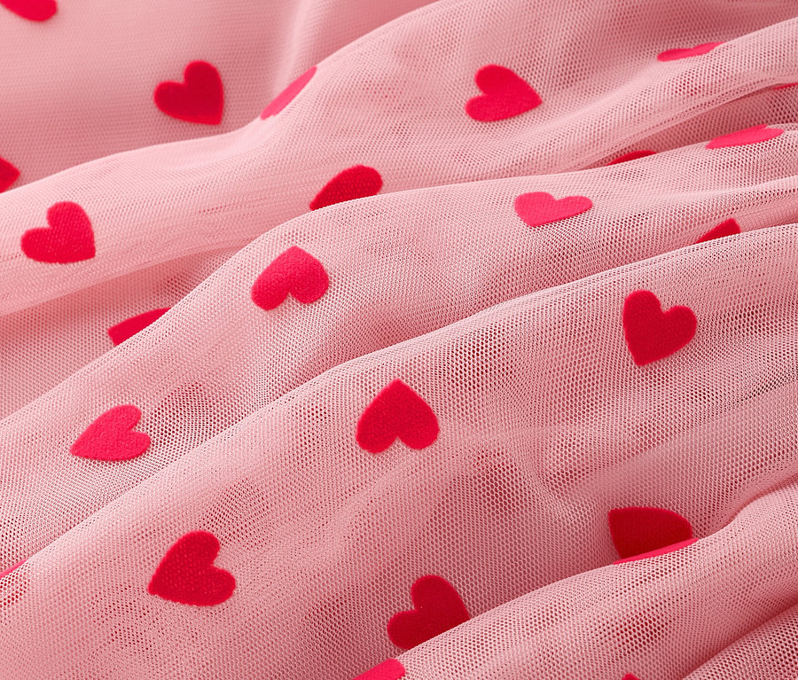 Közeli kép egy ráncolt, rózsaszín tüllszövetről piros szívekkel.