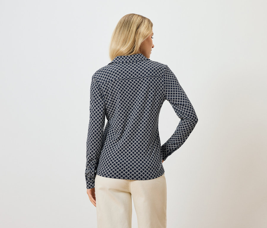 Hátulnézet egy szőke nőről, aki hosszú ujjú, kék mintás blúzt és világos nadrágot visel.