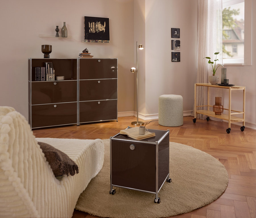 Modern nappali bézs kanapéval, nagy barna fém »CN3« komóddal 3 lehajtható rekesszel, kis barna fém »CN3« gurulós komóddal 2 lehajtható rekesszel kerek szőnyegen, buklé ülőkével és fa tálalókocsival.