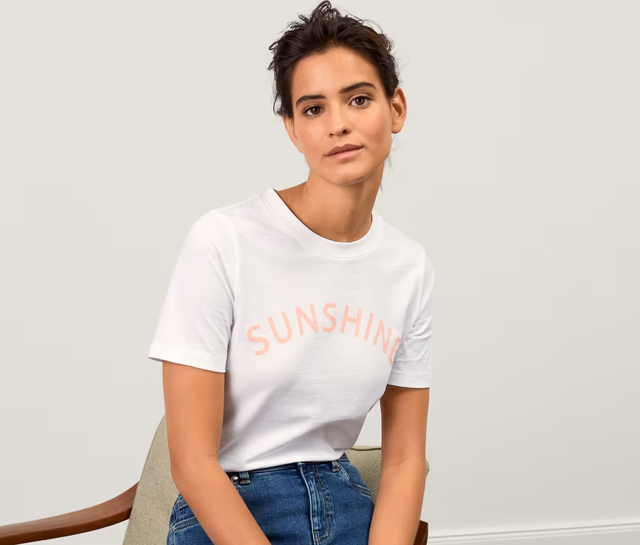 Nő ül egy széken, és egy fehér, "SUNSHINE" feliratú női pólót visel.