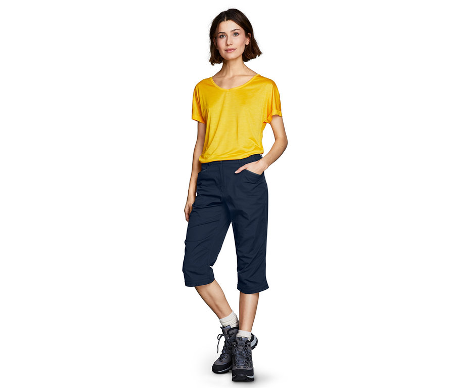 Egy nő áll sárga pólóban és sötétkék, 2 az 1-ben funkcionális nadrágban.