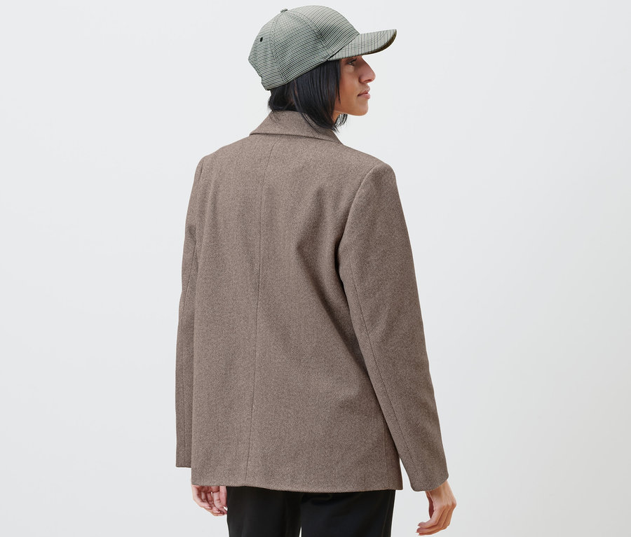 Nő blézerben és kockás sapkában jobbra néz.