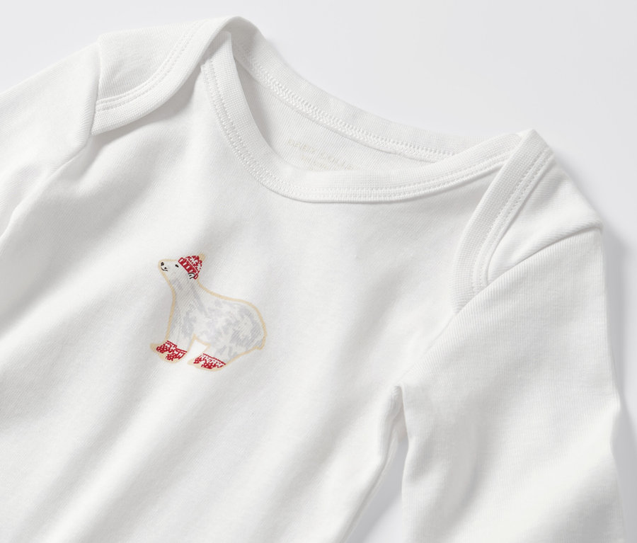 Egy kisgyerek hosszú ujjú body részlete, jegesmedve mintával, piros sapkával és zoknival.