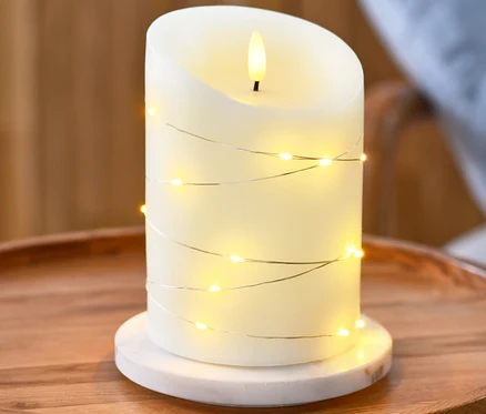 Egy LED-es valódi viaszgyertya mikroledes fényfüzérrel egy kerek fa asztalon áll.