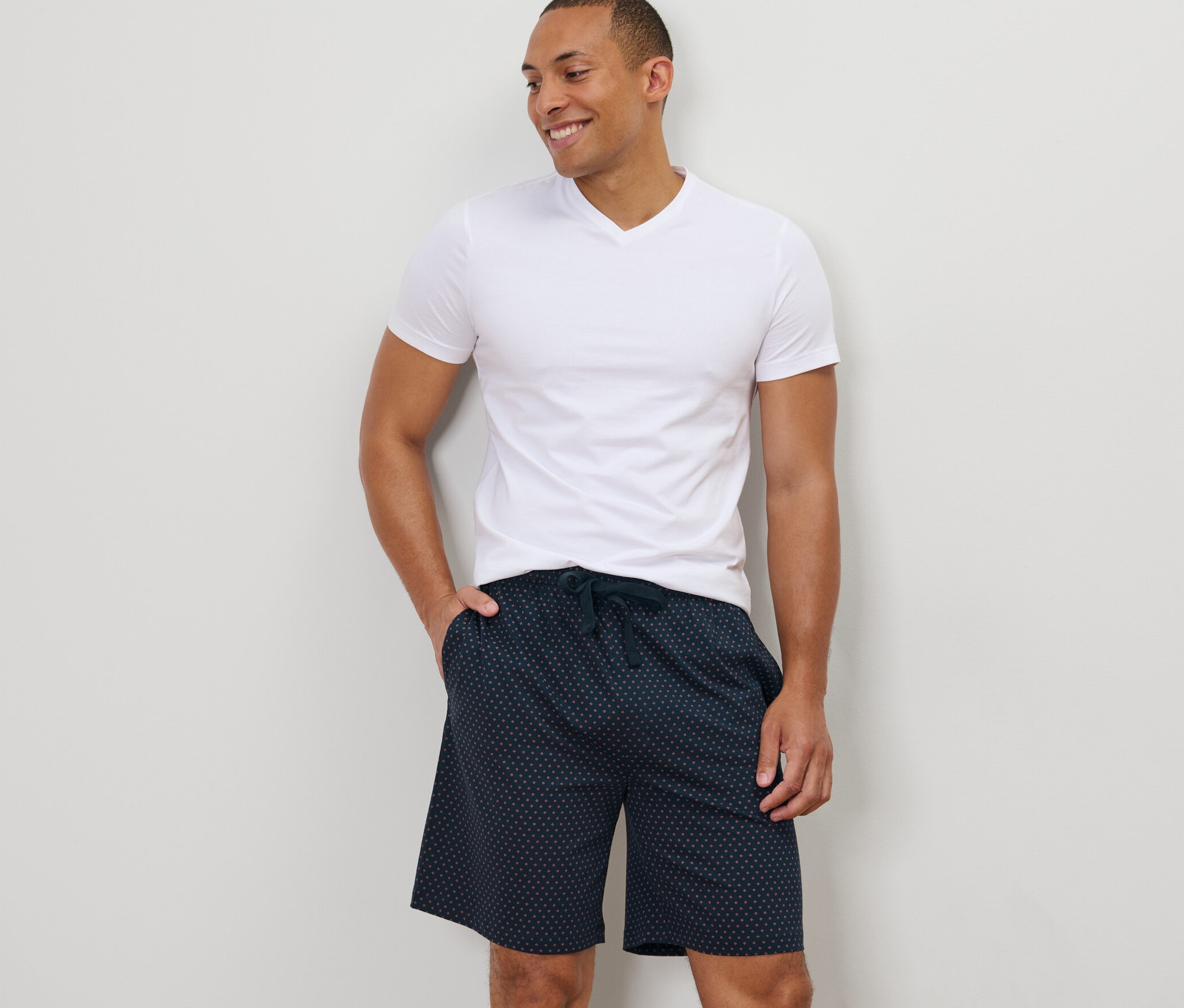 Férfi áll, keze a mintás, sötétkék férfi jersey rövidnadrág zsebében.