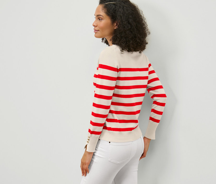Oldalnézet egy sötét, göndör hajú nőről, aki egy piros csíkos, finomkötésű pulóvert és fehér farmert visel.