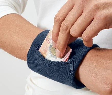 Egy kéz egy euró bankjegyet és egy érmét helyez egy kék biztonsági pénztárcába a csuklóján.