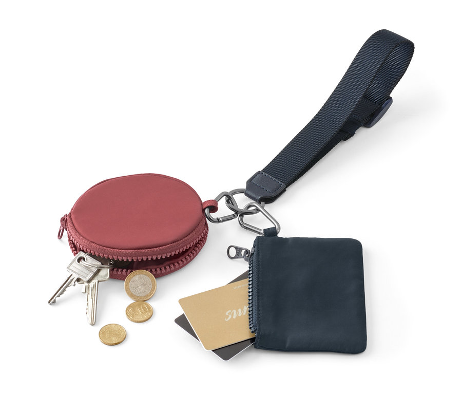 Bordó, kerek pénztárca kulcsokkal és érmékkel egy kék, cipzáras pénztárca mellett, kártyákkal és multifunkcionális kulcstartó pánttal.