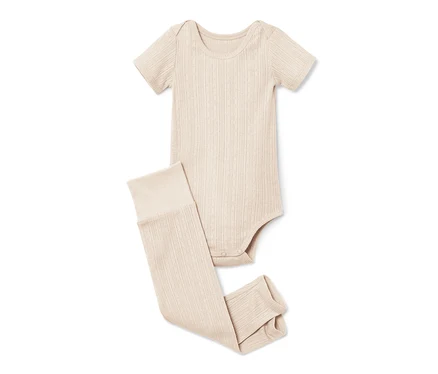Egy bézs baba body és leggings fekszik egy fehér háttéren.
