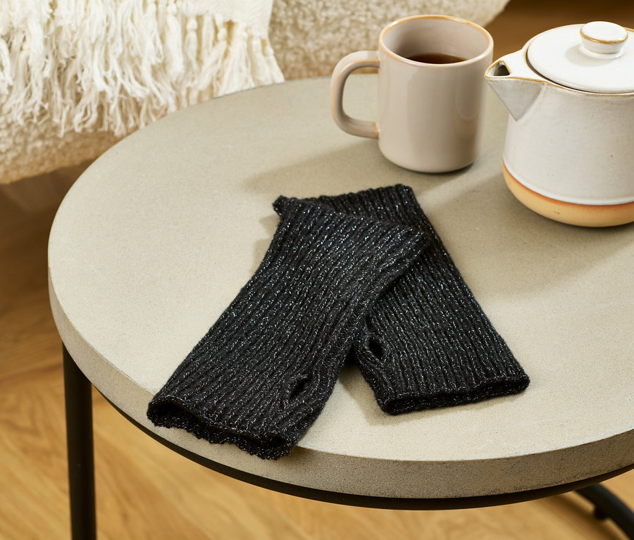 Az asztalon fekete, csillogó kötött csuklómelegítők, egy bögre és egy teáskanna látható.
