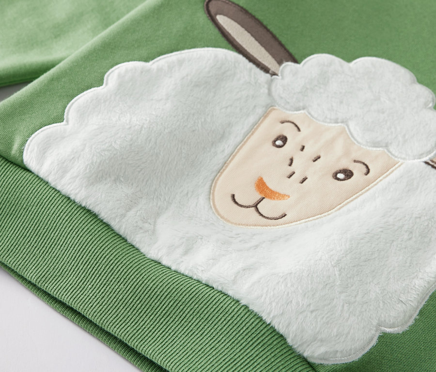 Egy zöld, bárányos kisgyerek szabadidőfelső részletgazdag képe.