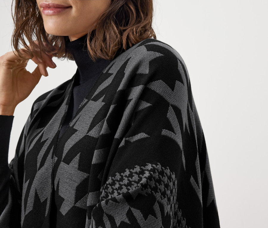 Egy fekete garbót és egy mintás, szürke és fekete pelerint viselő nő részleges képe.