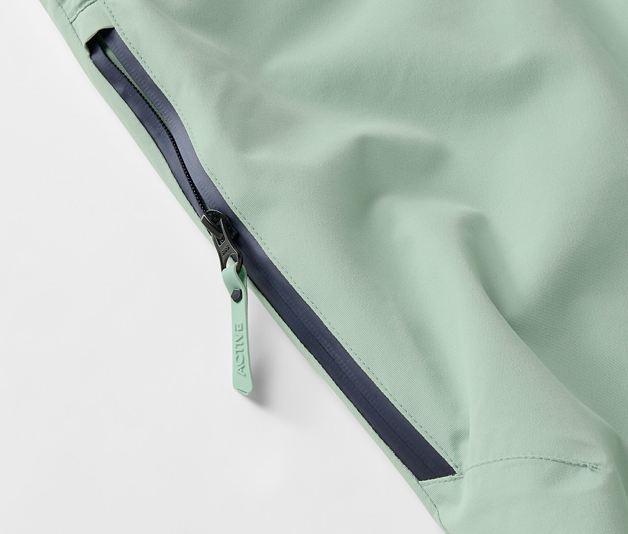 Világoszöld kabát részlete cipzárral és sötétkék szegéllyel.