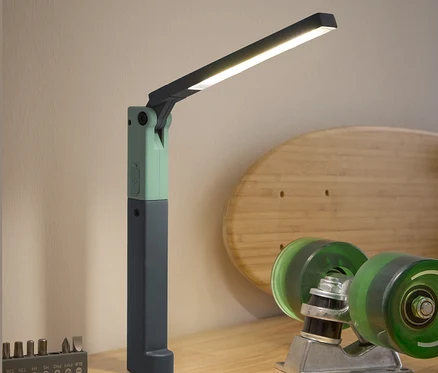 Egy LED-es munkalámpa, egy csavarhúzó, egy bitkészlet és egy gördeszka tartozékai láthatók egy fa asztalon.
