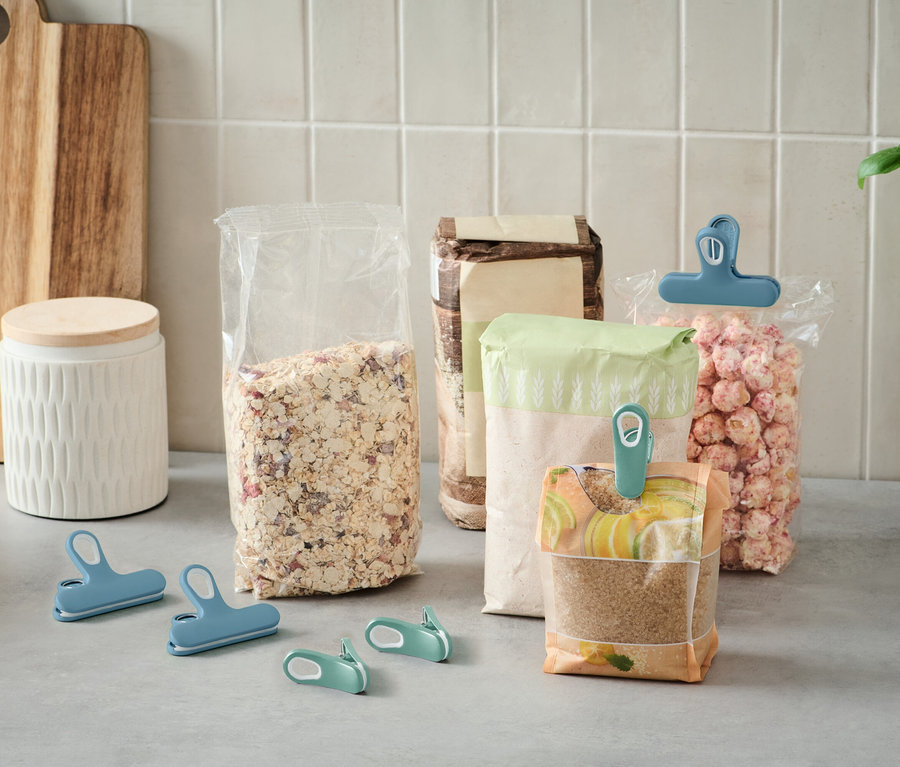 Számos nyitott élelmiszeres zacskó áll a konyhapulton, színes kapcsokkal lezárva.