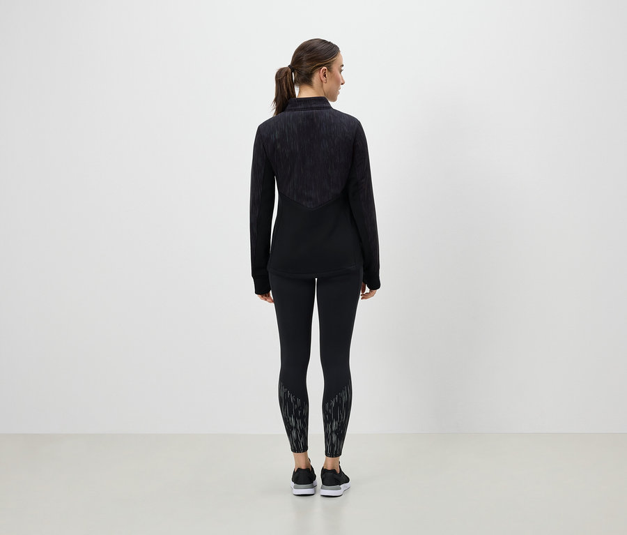 Egy nő háttal áll a kamerának, és fekete sportruházatot visel.