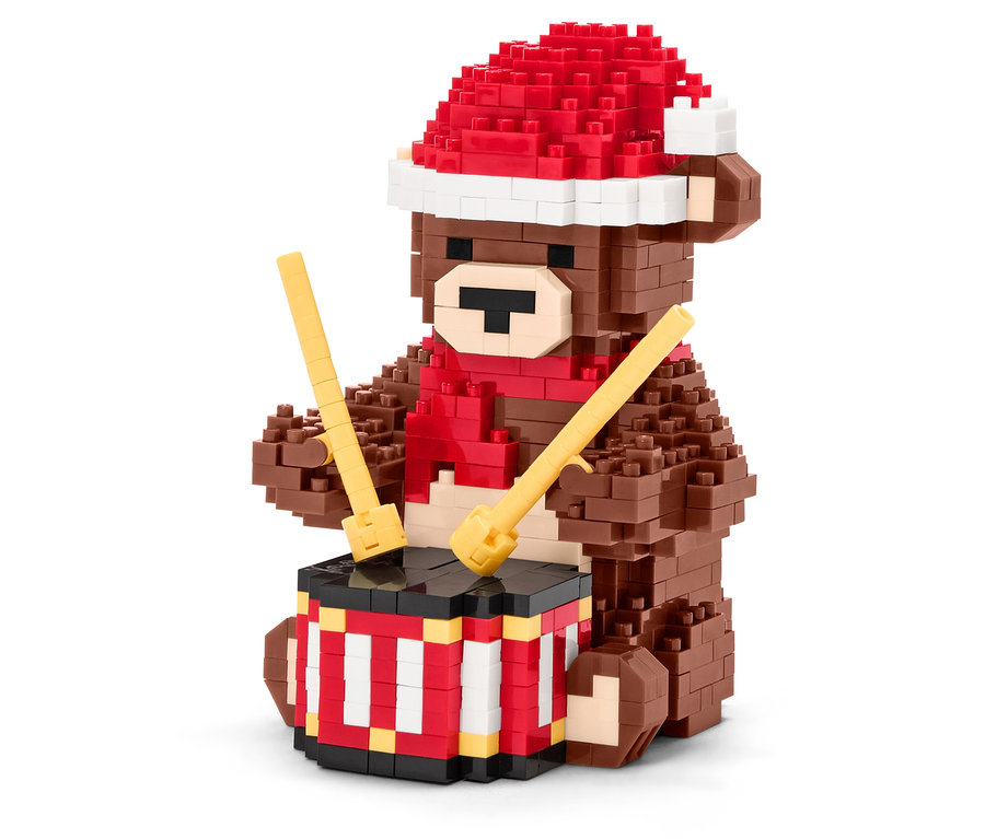 Egy barna építőkocka medve piros sapkával és sállal dobol ütőkkel.