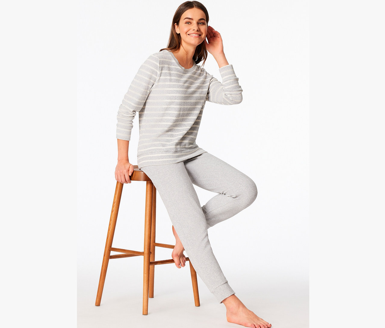 Nő ül egy fa székleten, szürke csíkos pizsamában.