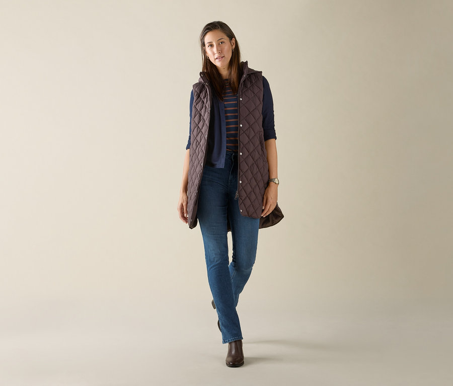 Nő visel egy hosszú, steppelt, sötétbarna kapucnis mellényt.