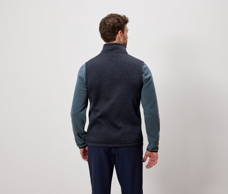 Hátulról látható férfi sötétkék mellényt és kék pulóvert visel.