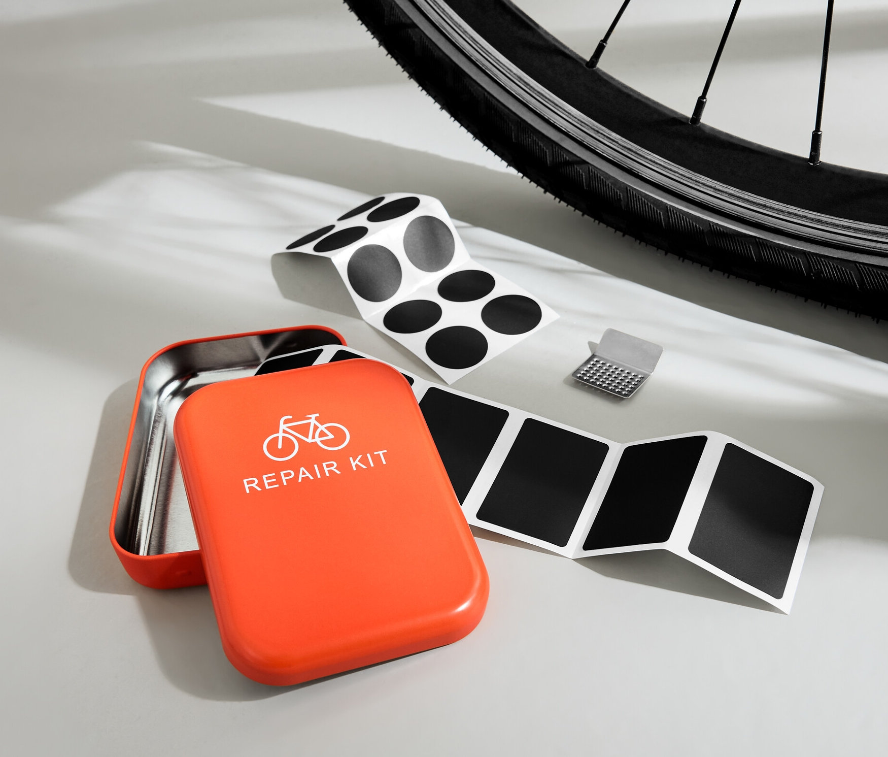 Nyitott narancssárga kerékpáros javítókészlet foltokkal és reszelővel egy kerékpárgumi előtt.