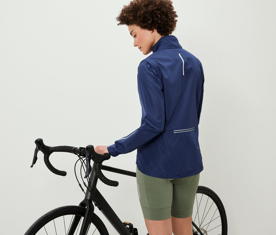 Egy nő egy kerékpár mellett áll és egy 2 az 1-ben kerékpáros kabátot visel.