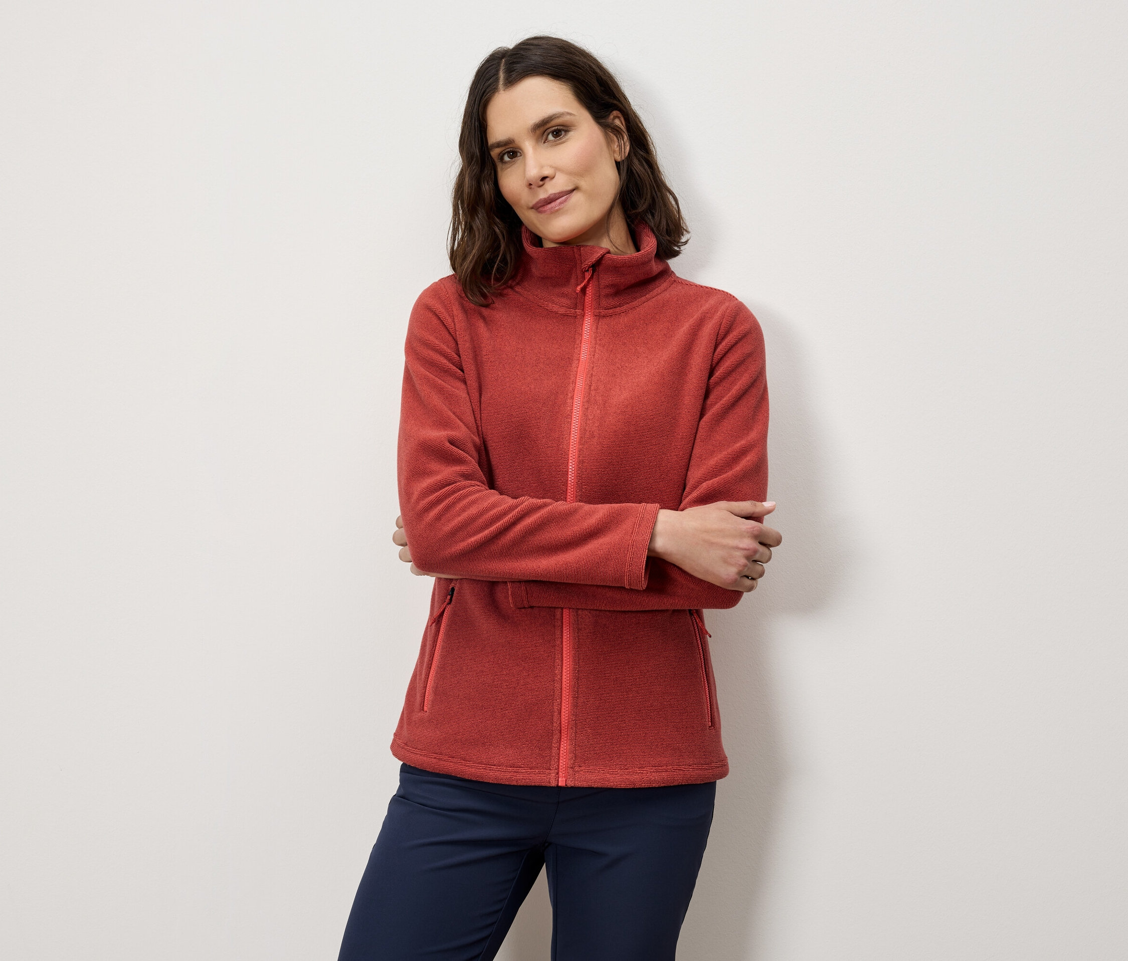 Nő keresztbe tett karokkal pózol narancssárga polár pulóverben és sötétkék nadrágban.